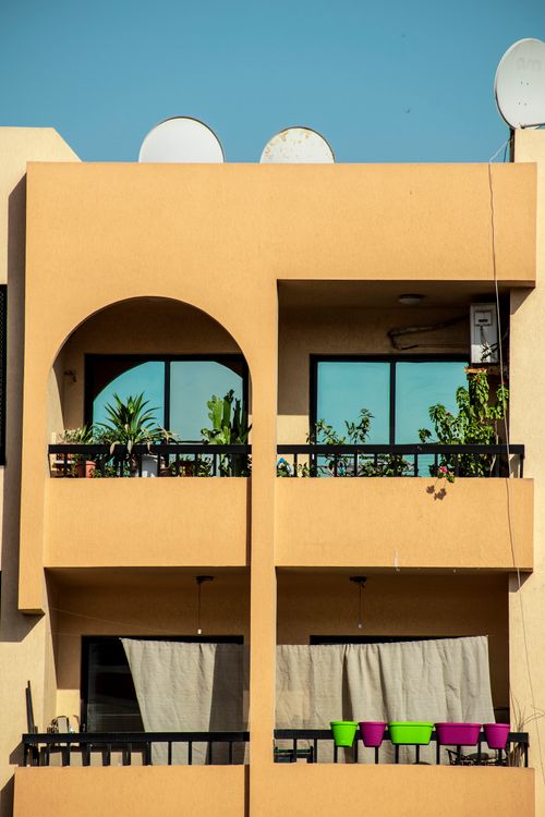 Free Contemporary urban apartment with balconies, potted plants, and a clear blue sky backdrop. Stock Photo
