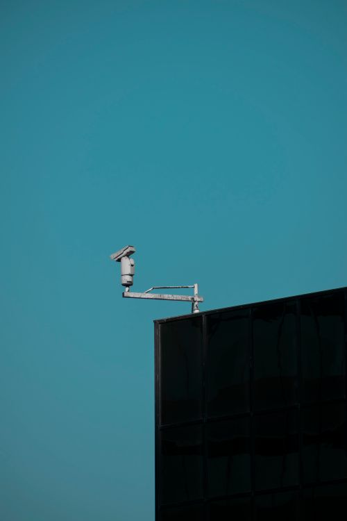 Free Modern architecture shot featuring a security camera and blue sky, showcasing urban surveillance. Stock Photo