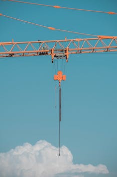 Orange tower crane suspended against a vibrant blue sky with clouds.