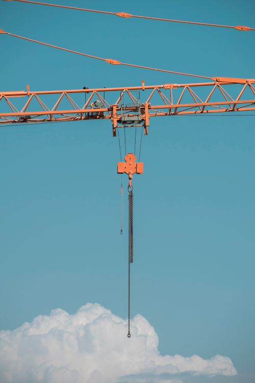 Free Orange tower crane suspended against a vibrant blue sky with clouds. Stock Photo