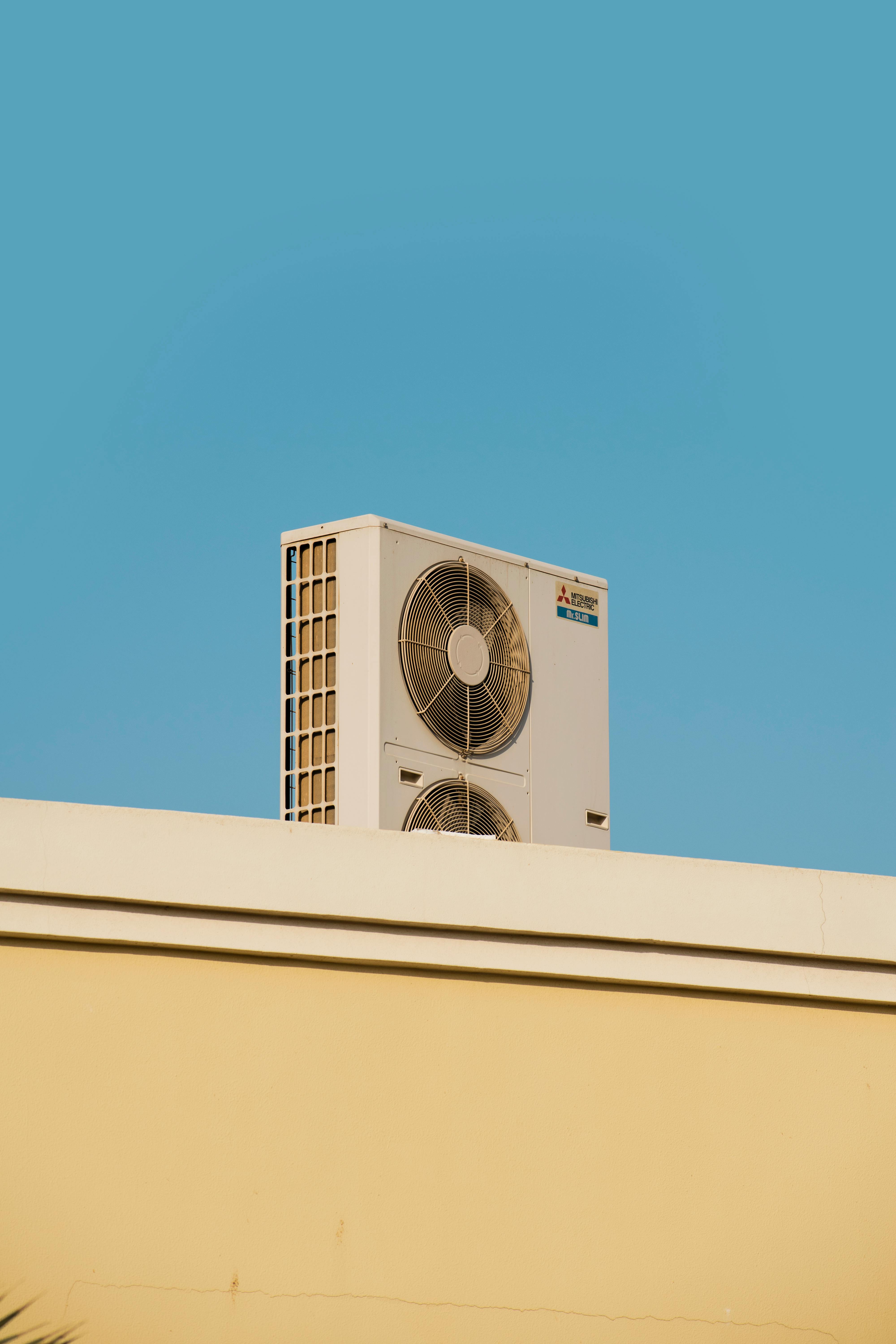 White air conditioner unit on a tan roof against a clear blue sky.