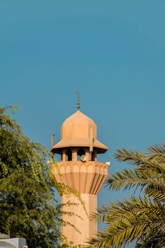 A traditional minaret tower framed by trees under a clear blue sky in Dubai, UAE.