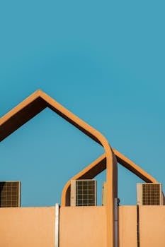 Modern architectural design featuring geometric roof structure and air conditioning units against a clear blue sky.