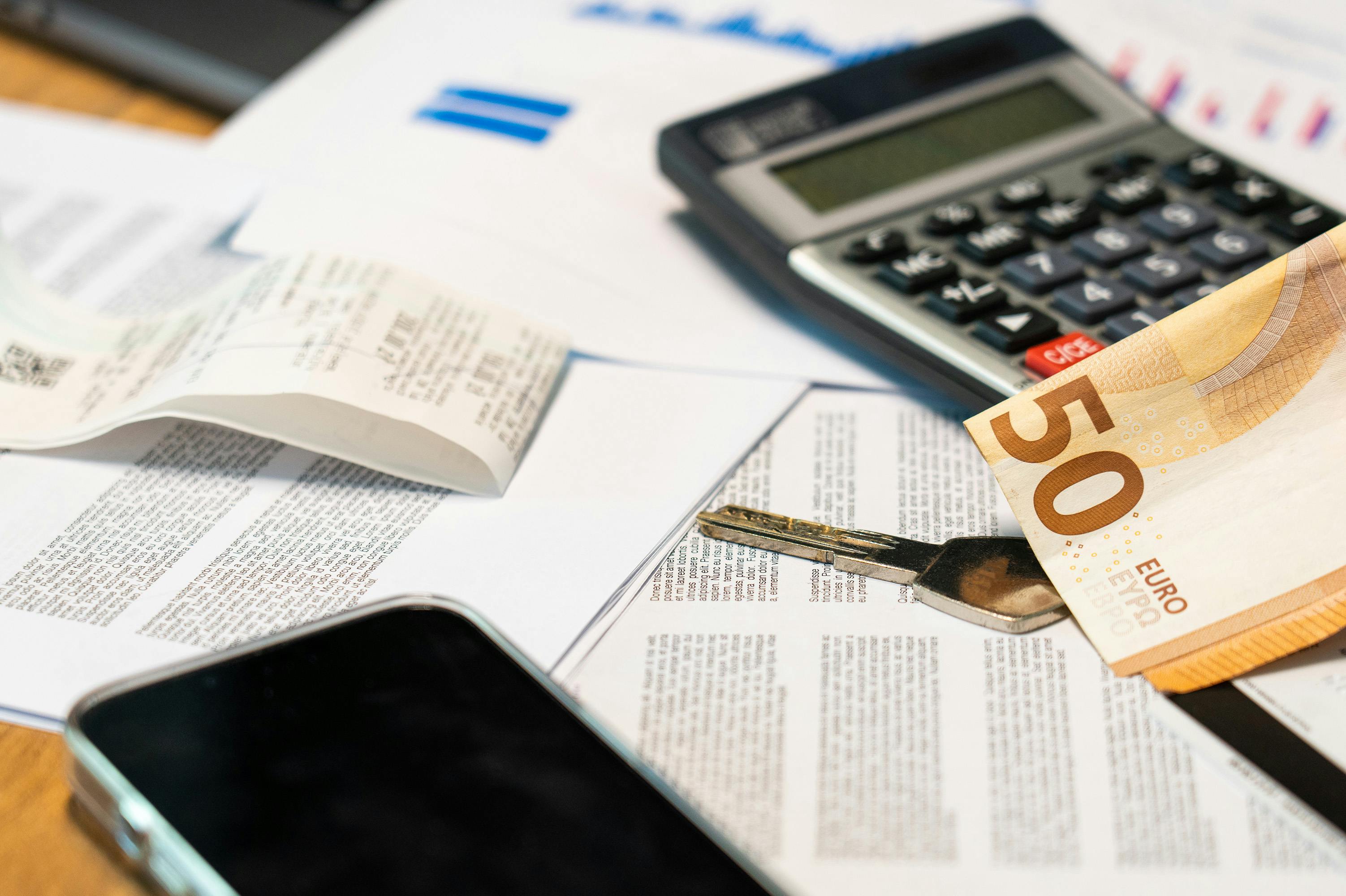 Euro banknote, keys and calculator on financial documents, highlighting travel or household expenses