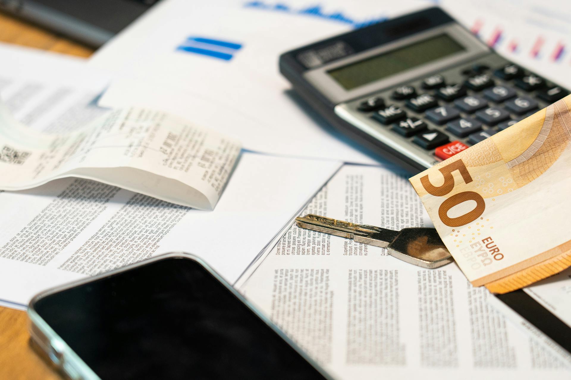 Flat lay of financial documents, euro note, calculator, smartphone, and key for budget management.