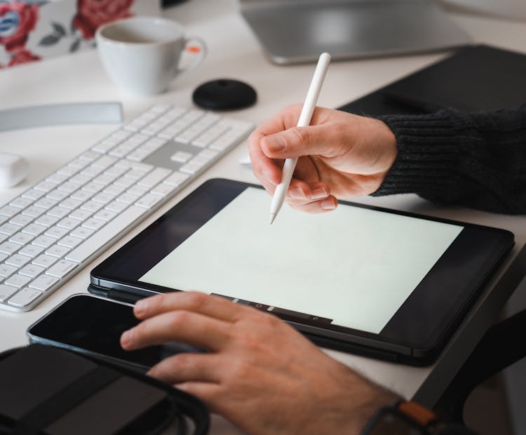 Person Holding Pen Above Tablet