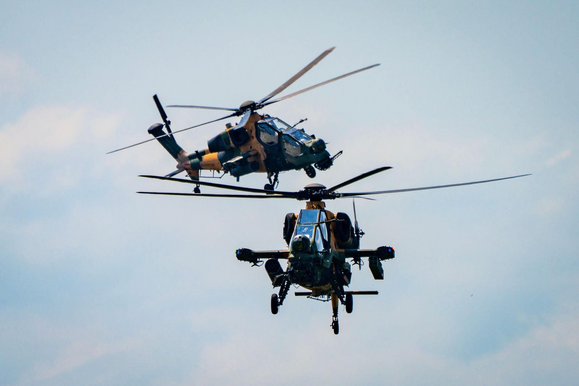 Two military helicopters flying in formation against a blue sky, showcasing aerial precision.