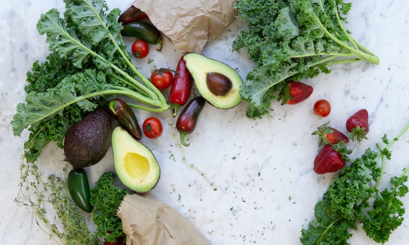 Flat-lay de alimentos low carb: abacate, folhas verdes, oleaginosas e vegetais frescos
