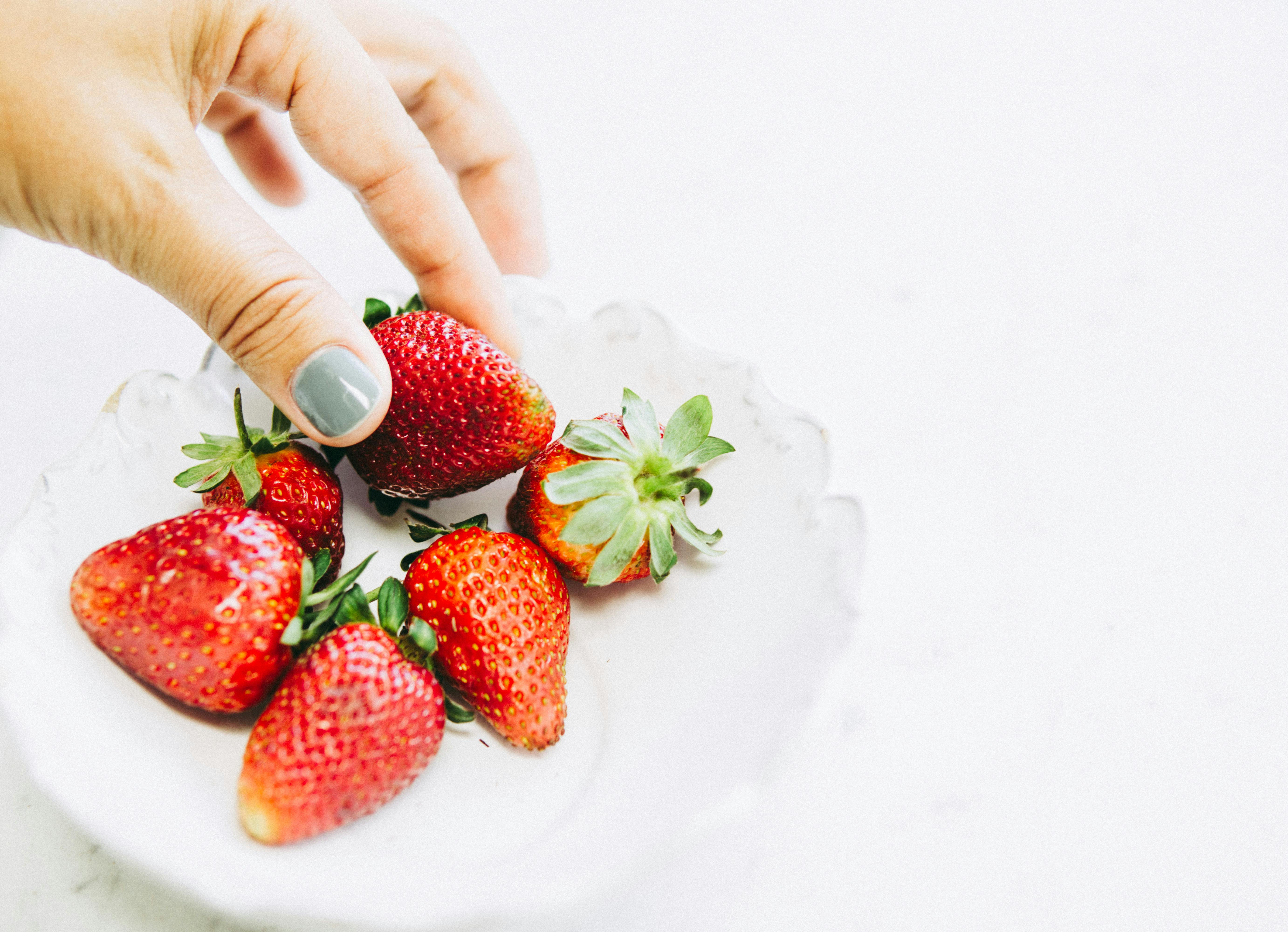 Bright and fresh strawberries being held over a white ceramic bowl, evoking a healthy lifestyle.