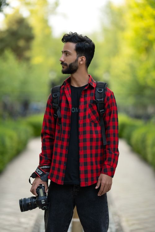 Free Young male photographer with camera, outdoors in a red plaid shirt. Ideal for creative and lifestyle themes. Stock Photo