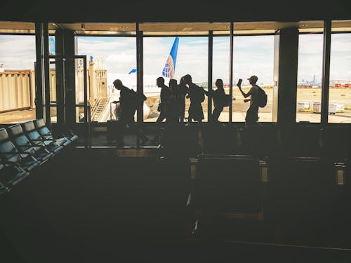 Grupo De Pessoas Andando Perto De Uma Janela De Vidro Transparente Com Vista De Um Avião Branco Estacionado Durante O Dia