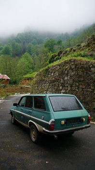 A classic vintage car parked on a misty mountain road surrounded by lush greenery.