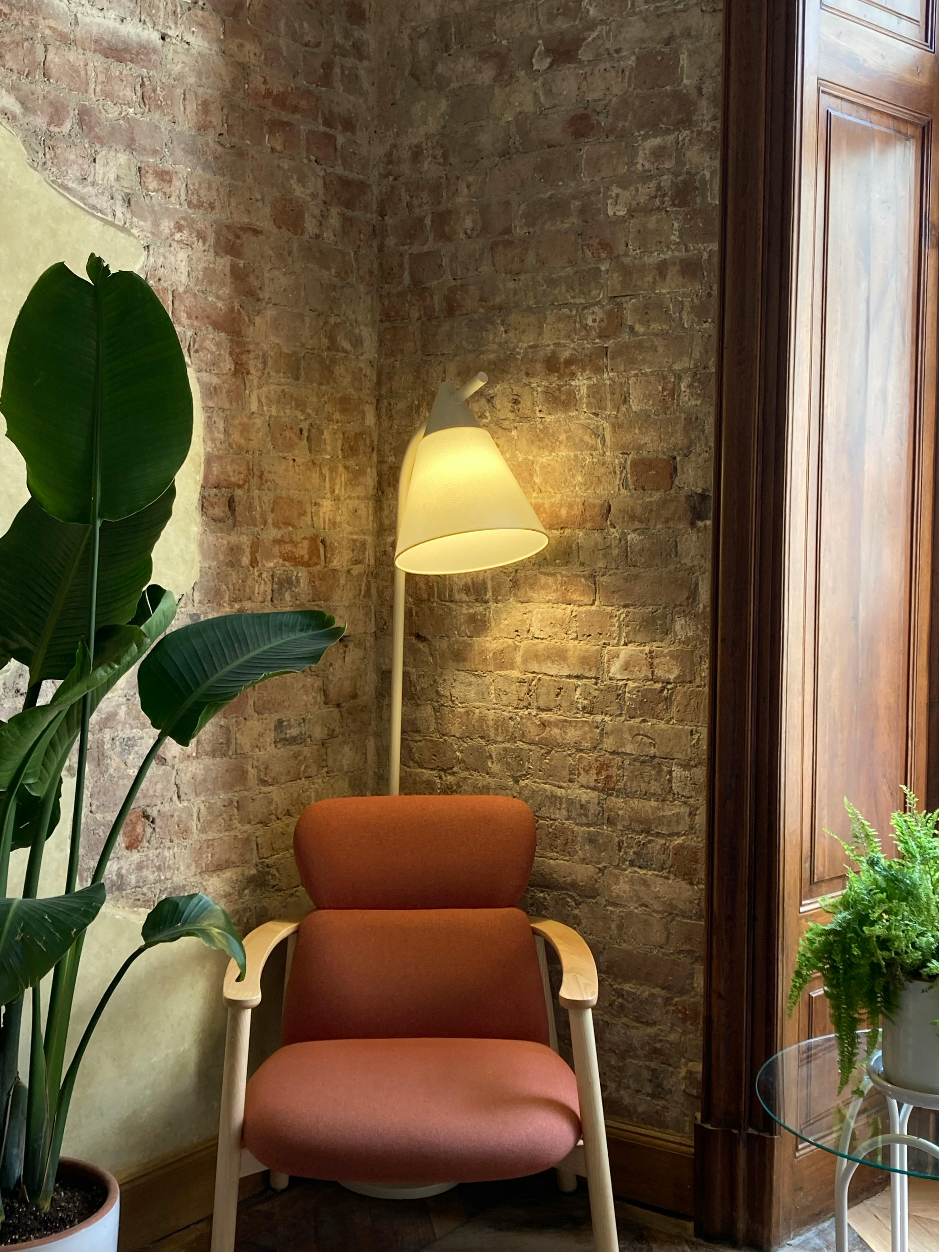 Free Warm and inviting living room corner with a stylish armchair, lamp, and houseplants against a rustic brick wall. Stock Photo