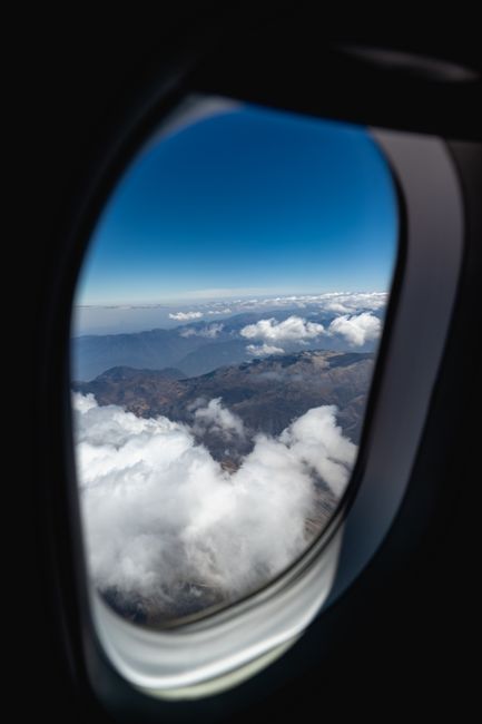 A breathtaking aerial view of clouds and mountains through an airplane window.