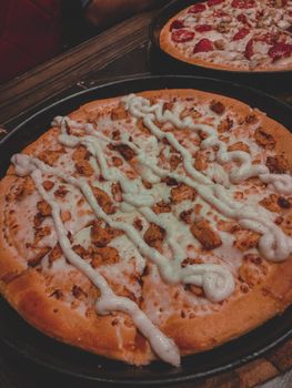 Close-up of a cheese pizza topped with a butter crust and sauce drizzle, served indoors.