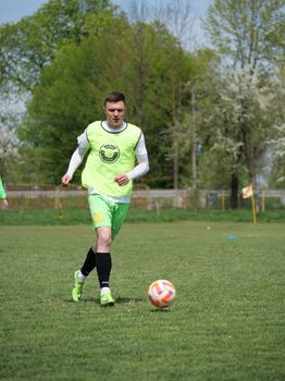 Male soccer player in action, dribbling a ball on a grassy outdoor field during a sunny day.