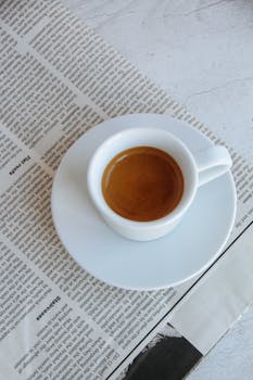 A fresh cup of espresso sits atop a newspaper, inviting relaxation and a leisurely moment.