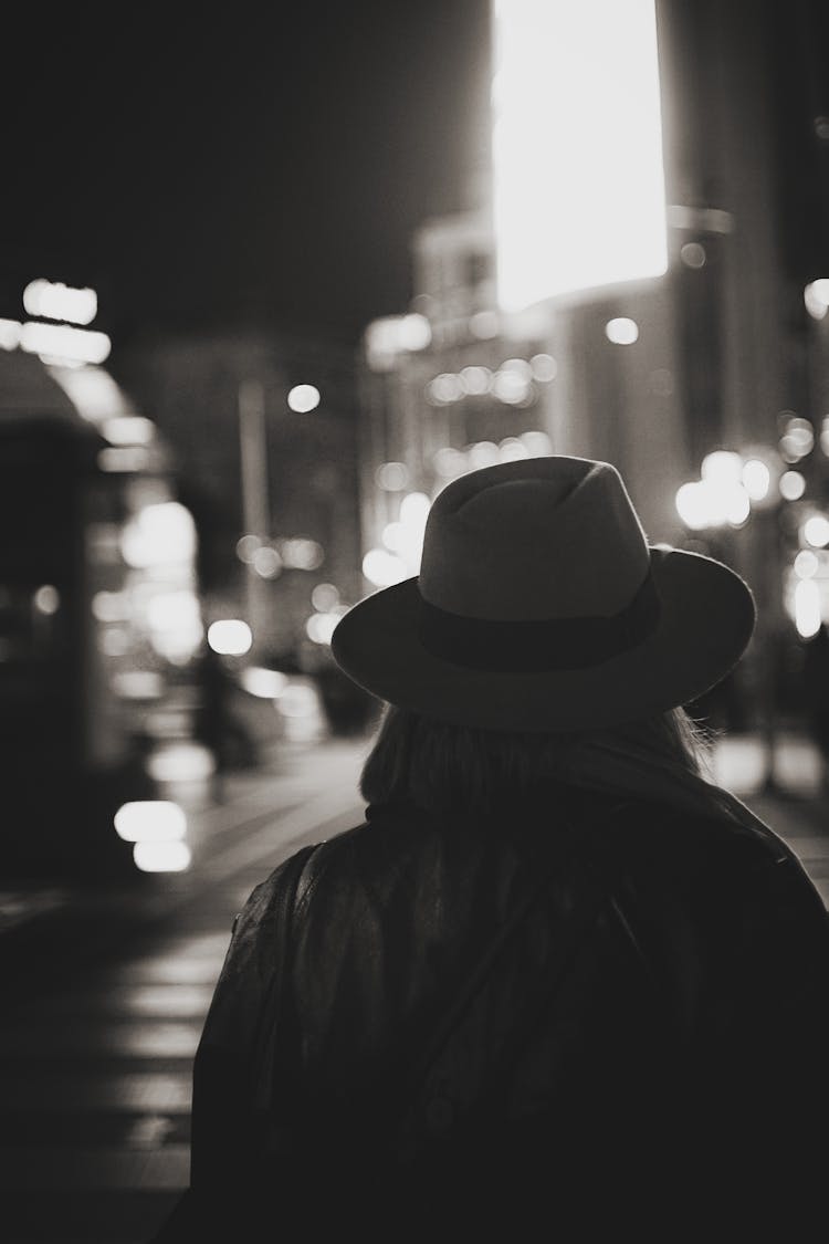 Back View Of A Woman In A Hat Walking On The Street At Night 