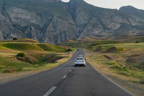 Free Picturesque view of a highway with cars surrounded by lush green hills and majestic mountains in summer. Stock Photo