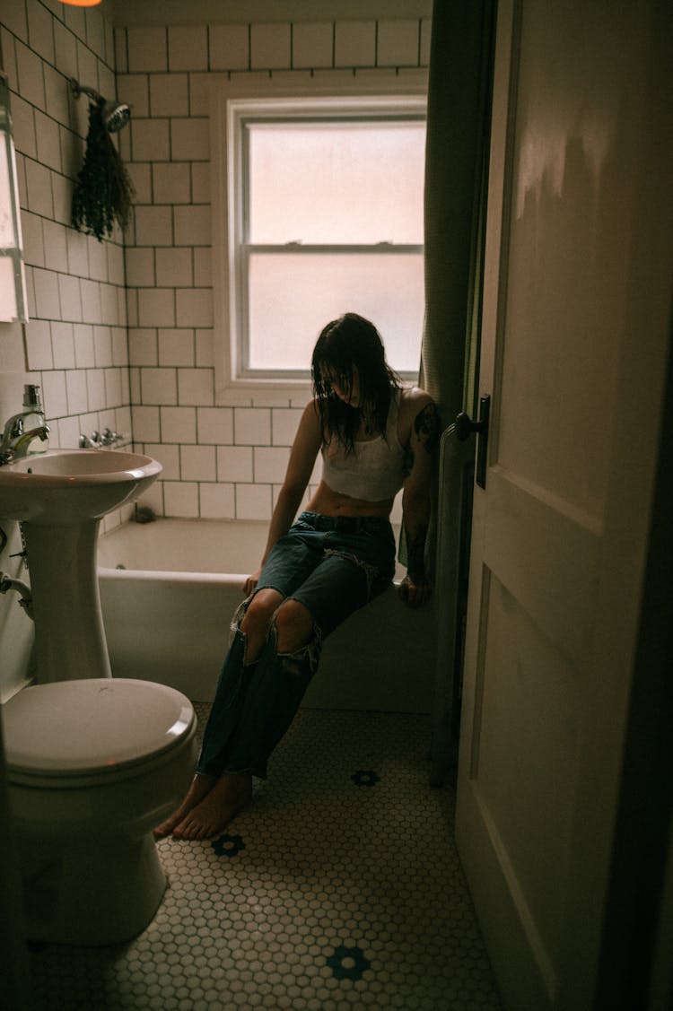 Young Woman Sitting On The Edge Of A Bathtub In The Bathroom 