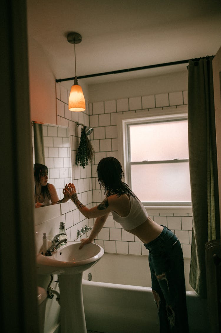 Young Woman Looking At Herself In A Mirror In The Bathroom 