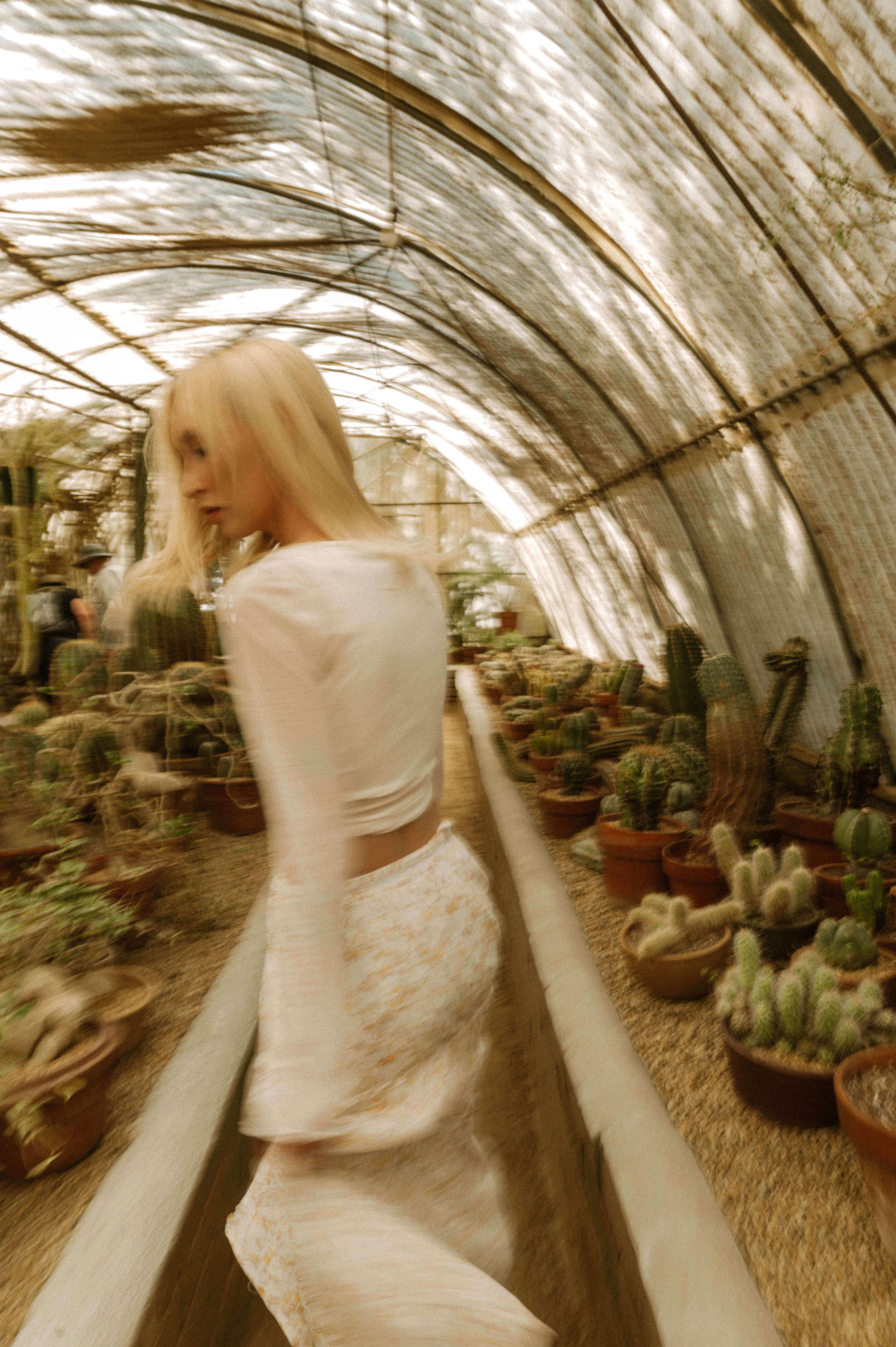 A woman in a flowing dress walks through a cactus-filled greenhouse in Palm Springs.