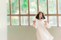 一位美丽的亚洲女性穿着休闲的白色服装，优雅地站在大窗户前