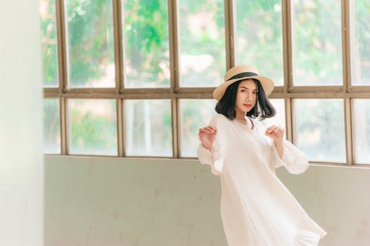 一位美丽的亚洲女性穿着休闲的白色服装，优雅地站在大窗户前