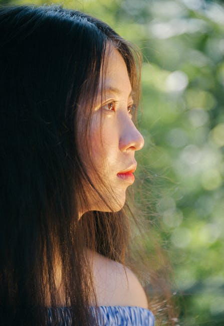 Profile view of a woman with long flowing hair against a blurred outdoor background.