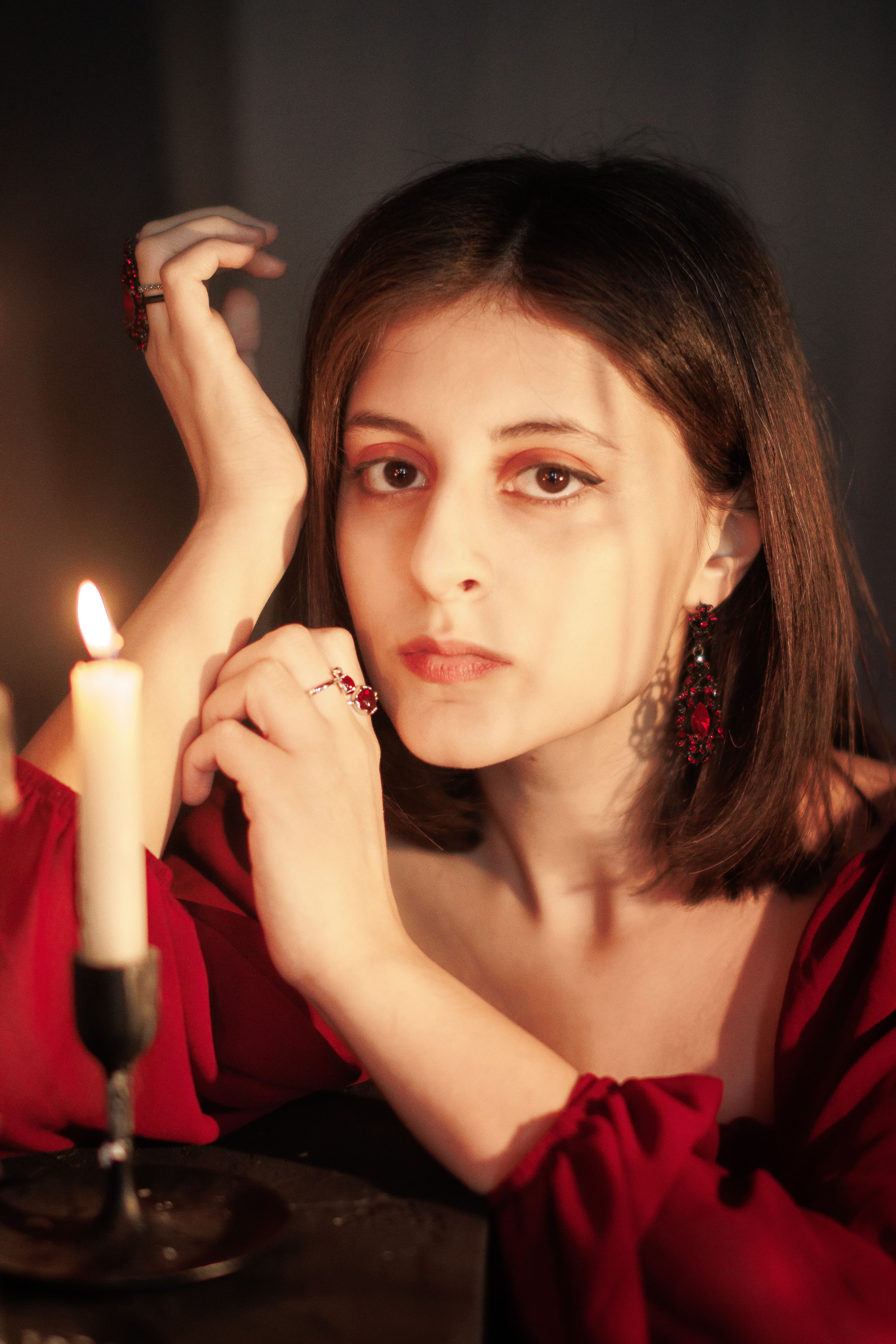 Elegant portrait of a young woman by candlelight wearing vintage red attire.