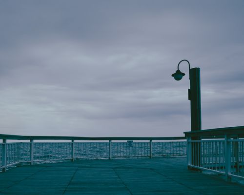 Free A serene view of an empty pier with an overcast sky, overlooking the calm sea. Stock Photo