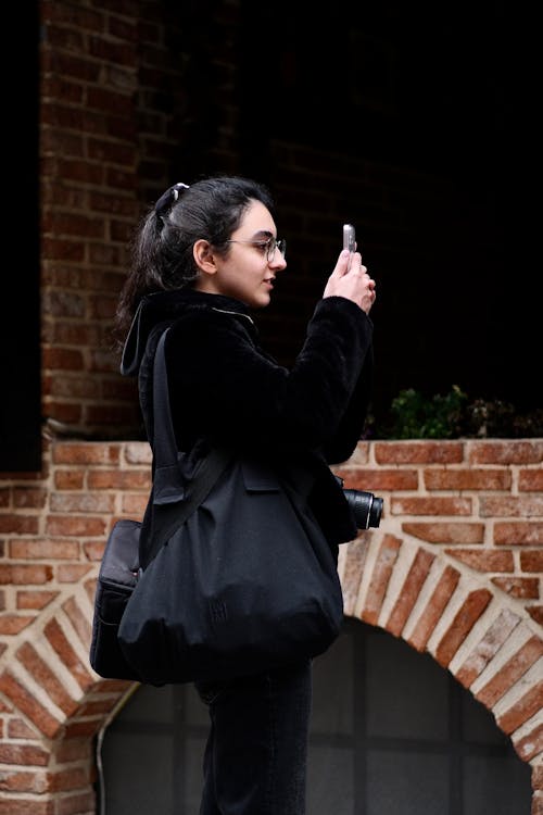 Woman with Camera around her Neck Taking Photo with Phone
