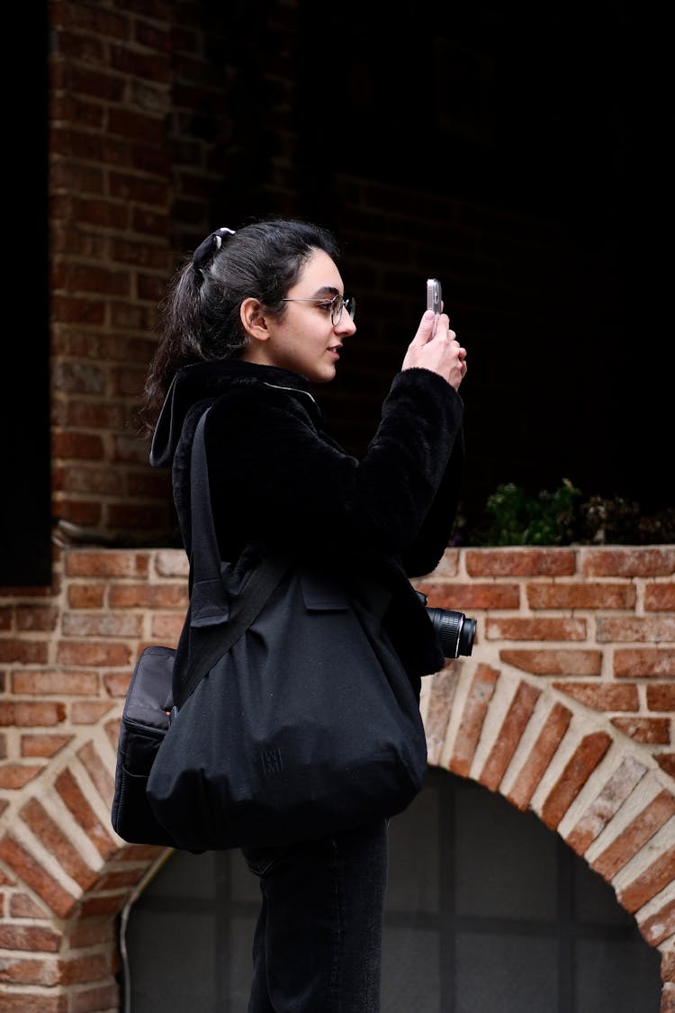 Woman With Camera Around Her Neck Taking Photo With Phone