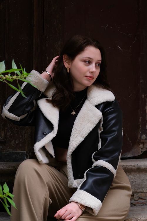 Free Young woman in a chic leather and fur jacket posing stylishly outdoors. Stock Photo
