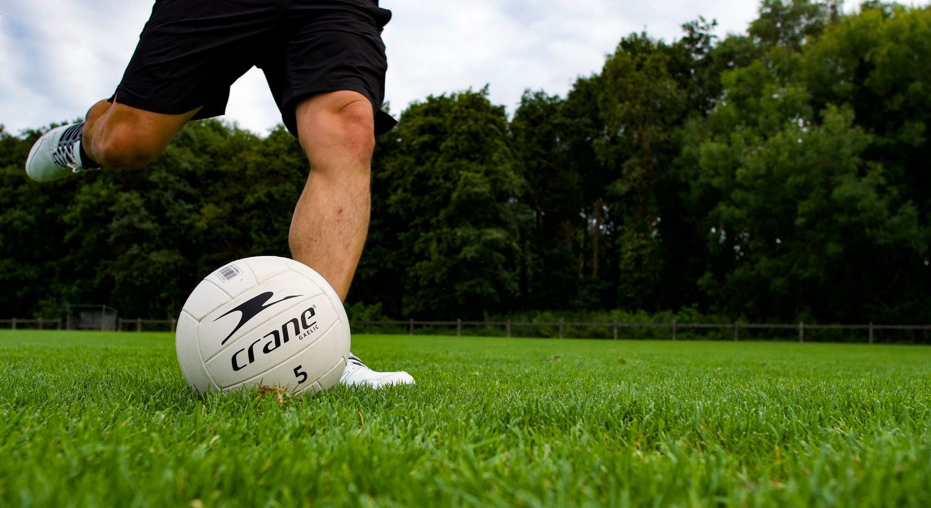 Close-up of a male athlete kicking a football on a lush green field. Focus on legs and ball.
