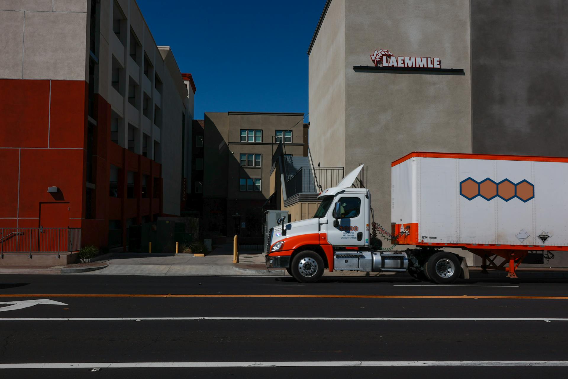 A delivery truck parked on a city street under bright sunlight in front of modern buildings.