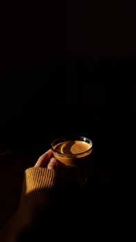 A person holds a warm drink in a dimly lit room, creating a cozy ambiance.