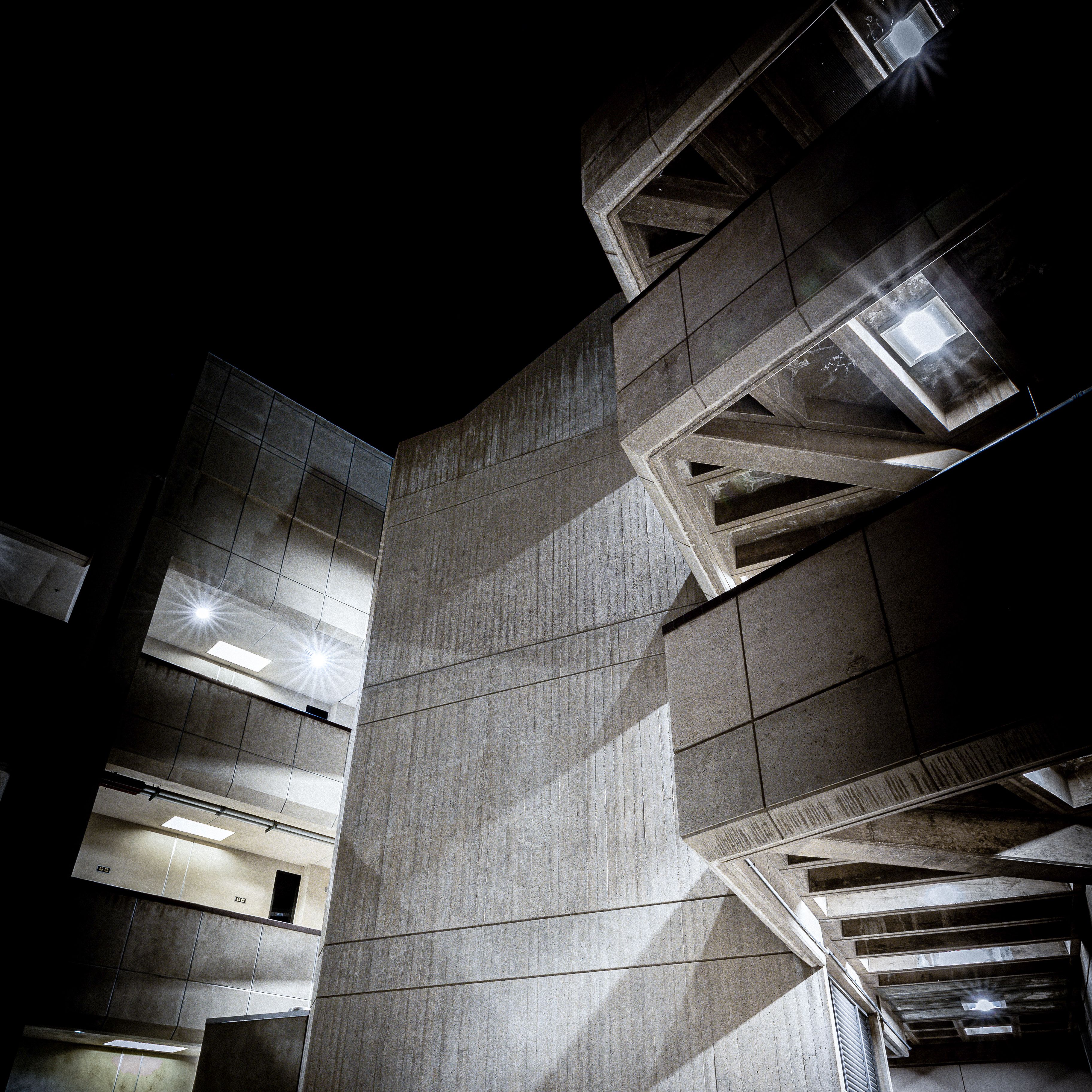 A striking low angle view of modern concrete buildings against the night sky, showcasing unique geometric designs and lighting.