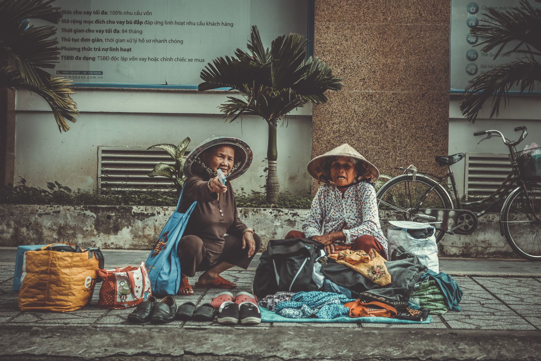 Two elderly street vendors selling clothing and accessories on an urban sidewalk.