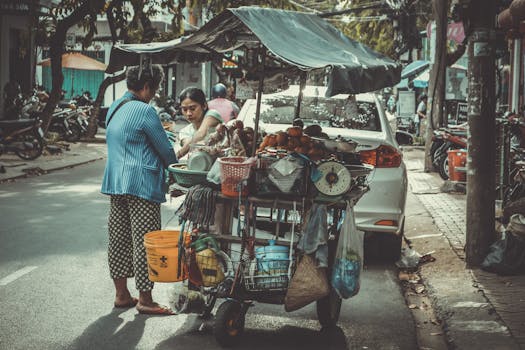 Two female vendors selling produce from a mobile cart on a busy street in Vietnam.