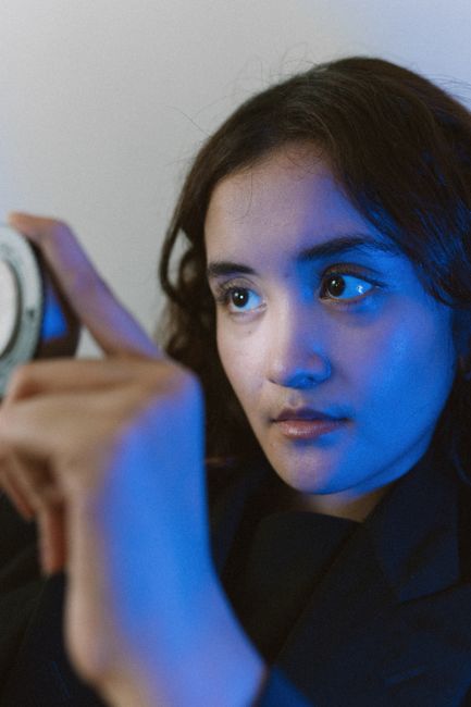 Close-up of a woman with long dark hair holding an object in blue lighting indoors.