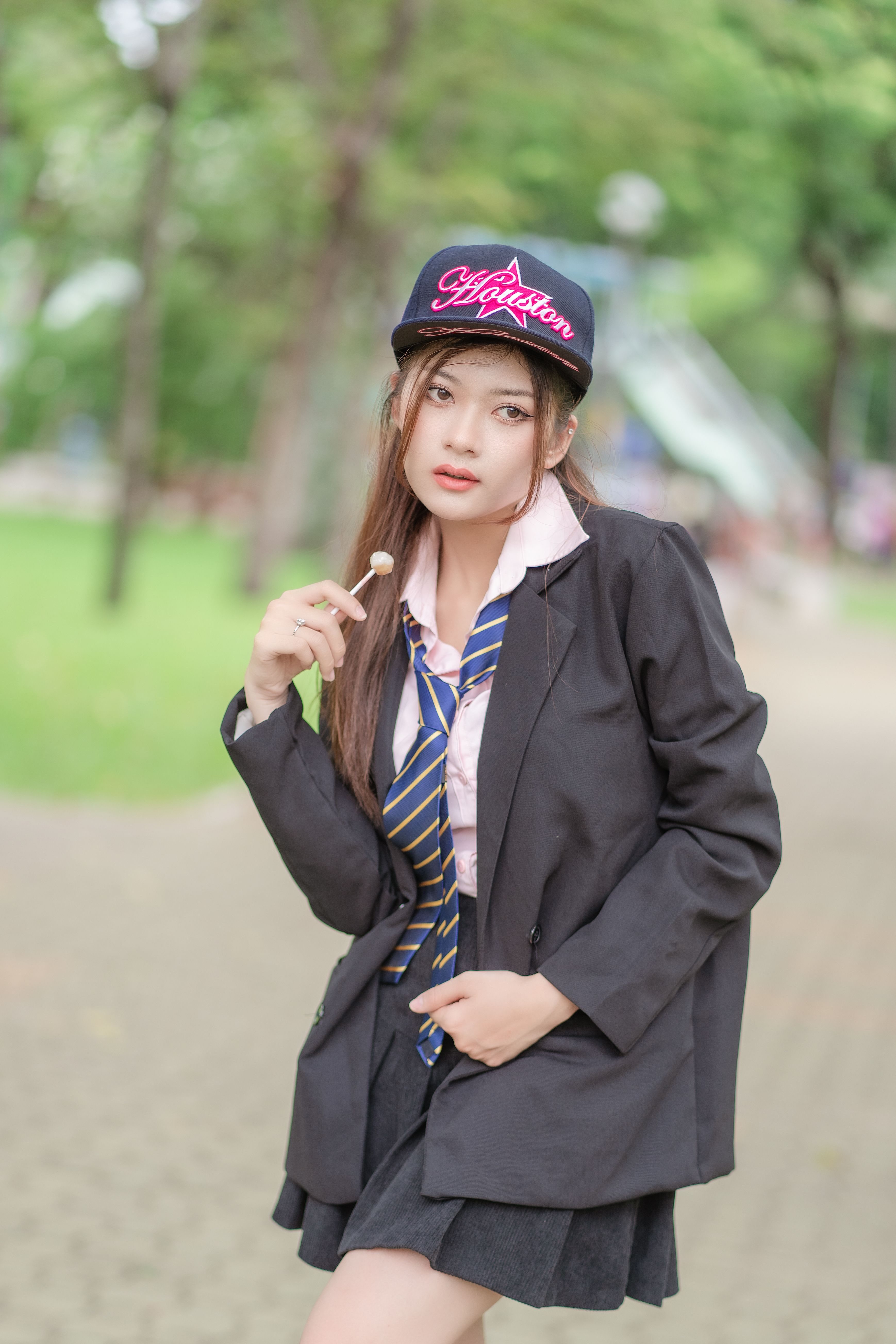 Stylish woman in black suit and cap posing with a lollipop outdoors.