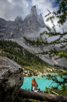 碧绿的湖边坐着一位红发女子，四周是引人注目的山峰和郁郁葱葱的绿色植物