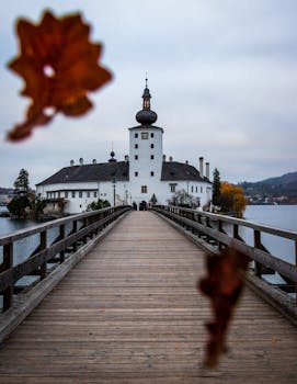 一座历史悠久的城堡风景如画，由一座点缀着秋叶的木桥连接