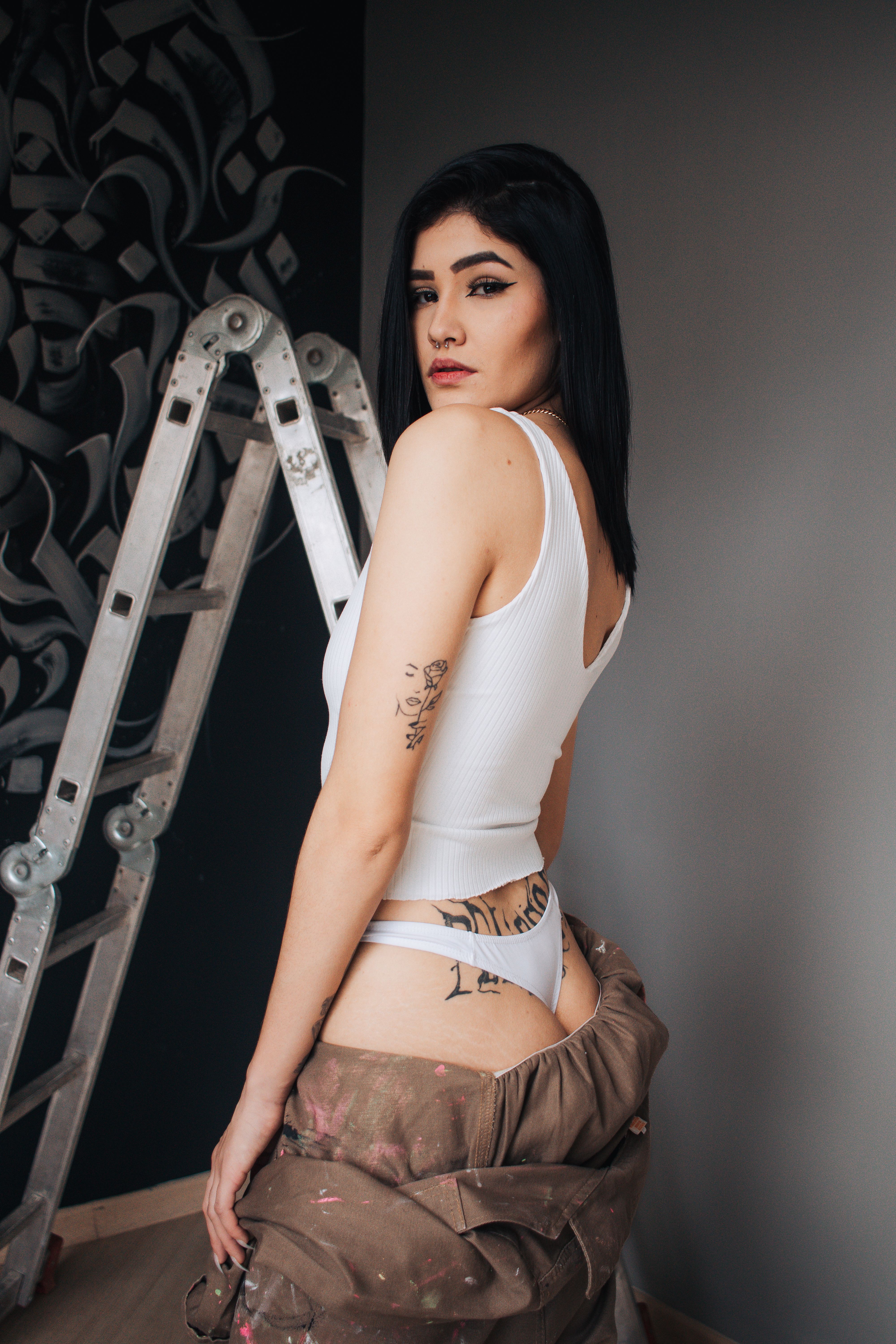 Tattooed woman in lingerie leaning against a ladder in a renovated room.