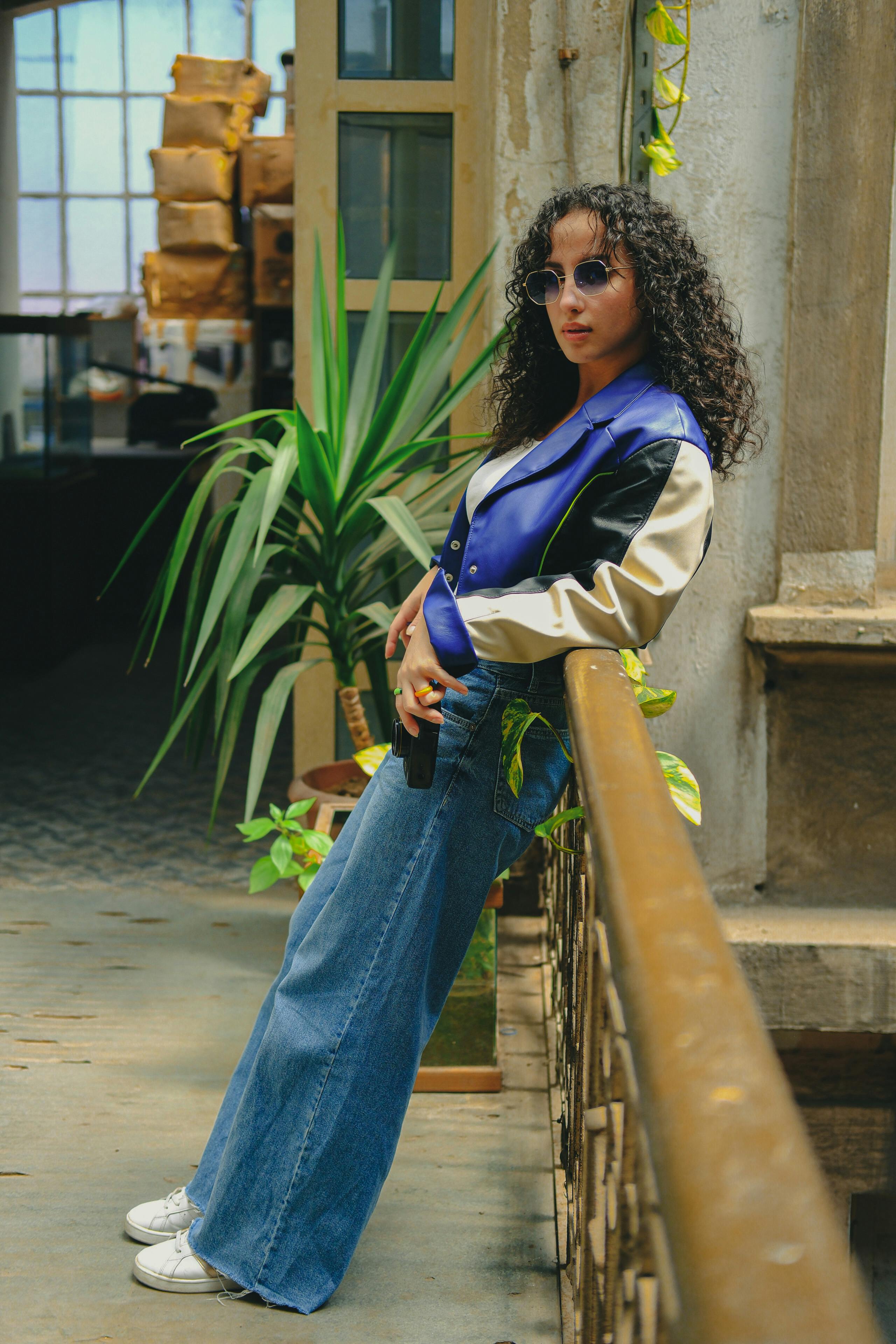 a woman in jeans and a jacket leaning against a railing