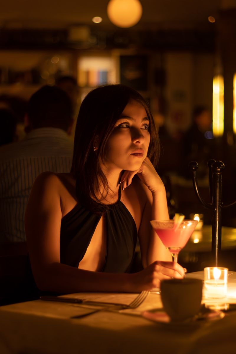 Young woman in a stylish dress with a cocktail at a candlelit bar