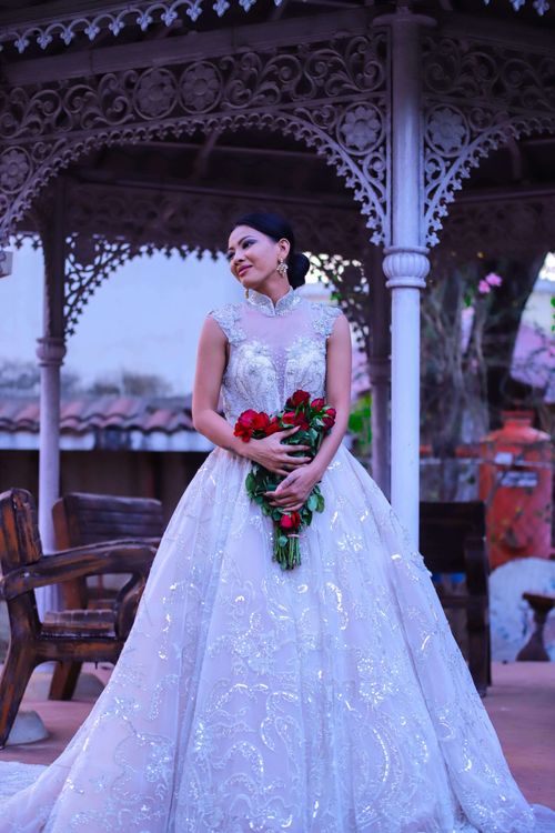 Free Beautiful bride in white gown in a decorative gazebo holding a red bouquet. Stock Photo