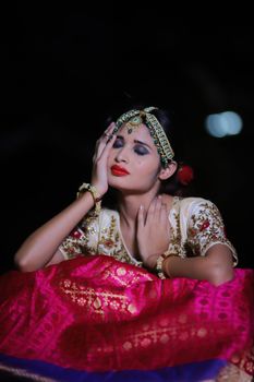 Graceful woman in vibrant traditional dress with intricate jewelry and makeup posing serenely.
