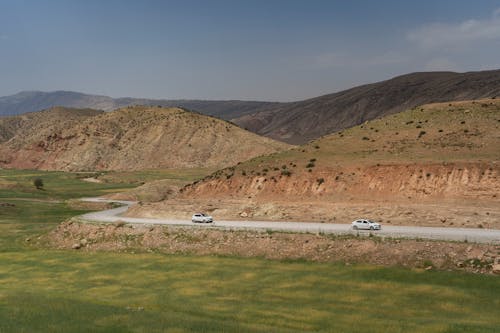 Two Cars Driving along a Winding Road with Hills in the Background